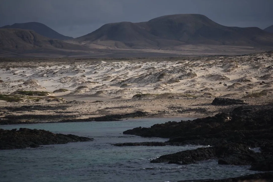 White dunes and black lava rocks under a heavy stormy sky
