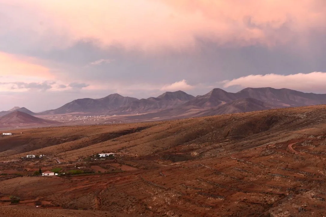 Pink clouds drifting over brown volcanic mountains