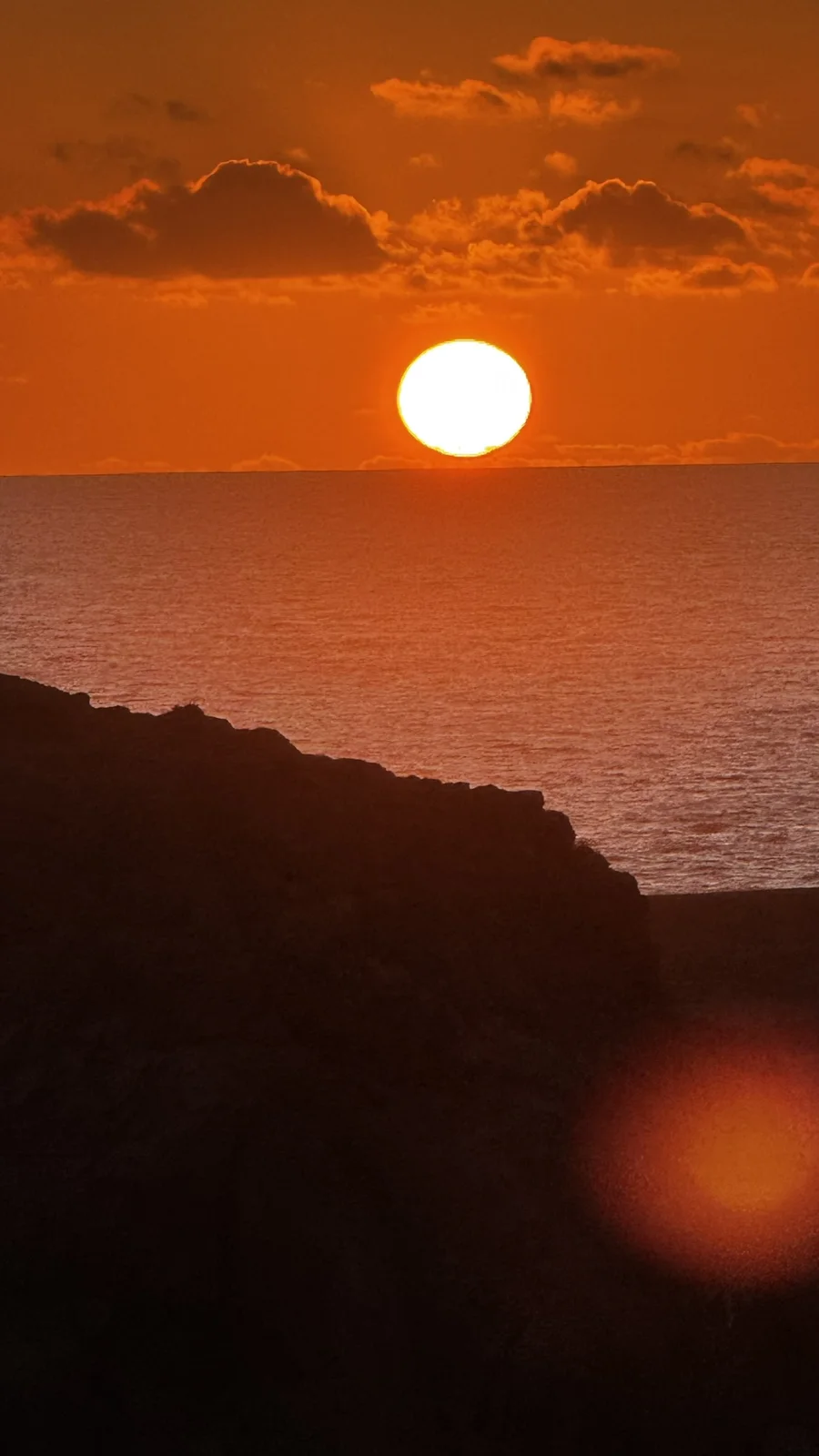 The sun setting into the Atlantic behind a dark cliff